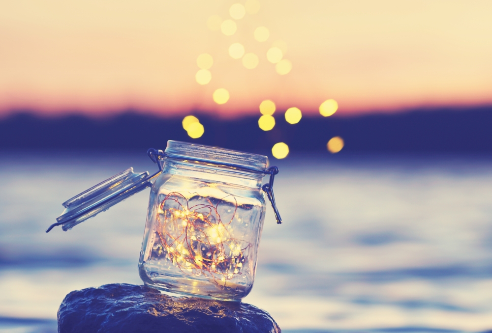 Ein Glas mit einer Lichterkette am Strand während des Sonnenuntergangs.